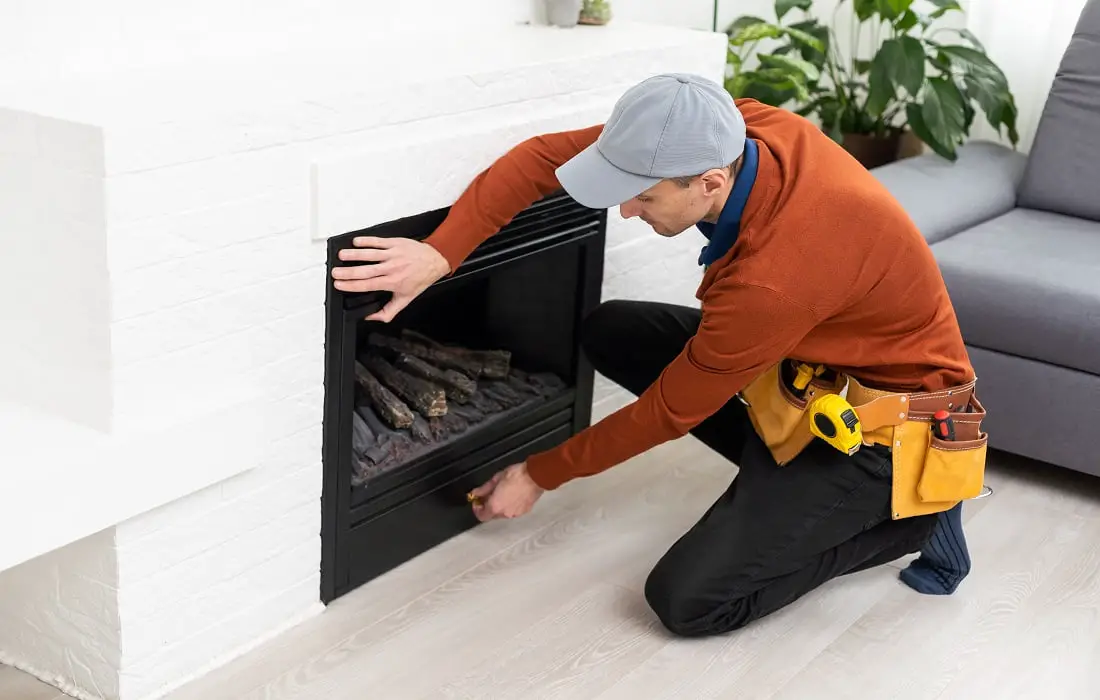 Professional-technician-sealing-electric-fireplace-with-caulk-near-white-wall-in-room